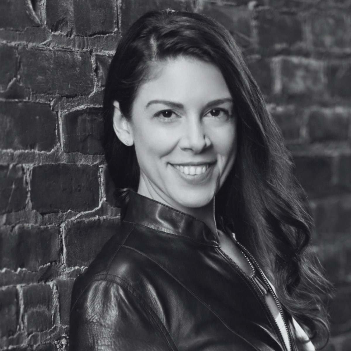 Smiling woman with long, dark hair against a light background. She's wearing a dark top, and the photo is in black and white, conveying a friendly tone.