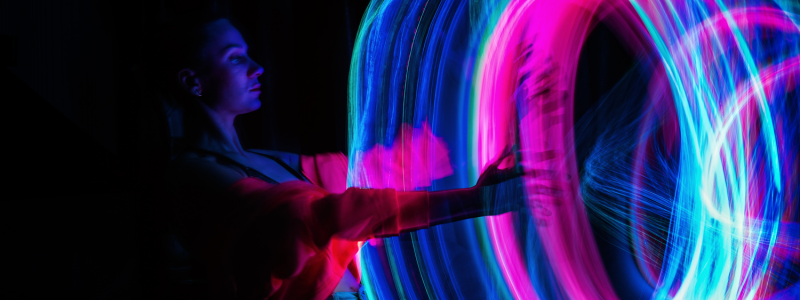 A woman in profile holds vibrant neon light trails of blue and pink that swirl around her.
