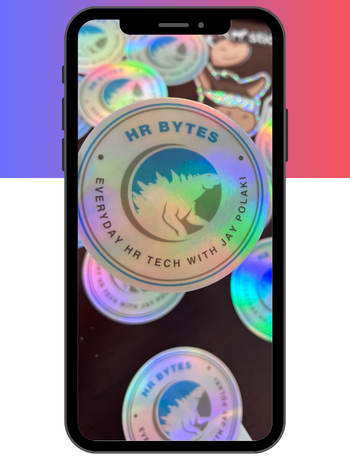 Holographic stickers reading 'HR Bytes, Everyday HR Tech with Jay Polaki' are displayed on a smartphone screen, creating a vibrant, reflective pattern.