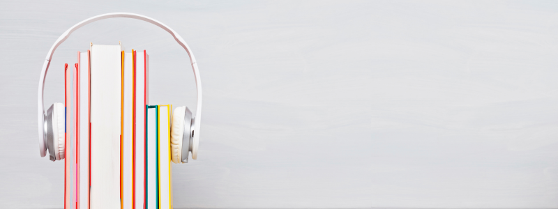 Row of colorful books upright with white headphones resting on top against a soft gray background, symbolizing audiobooks and learning.