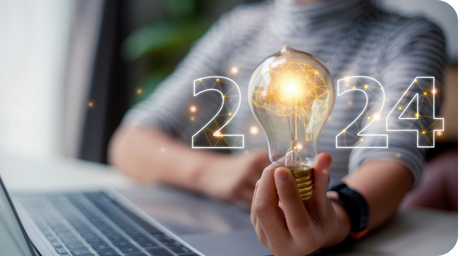 A person holds a glowing light bulb in front of a laptop, symbolizing creativity and innovation. The numbers '2024' are overlaid, conveying a futuristic theme.