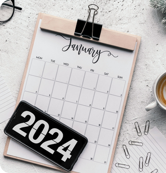 Clipboard with January 2024 calendar, smartphone displaying '2024,' scattered paper clips, and a coffee cup on a light textured surface.