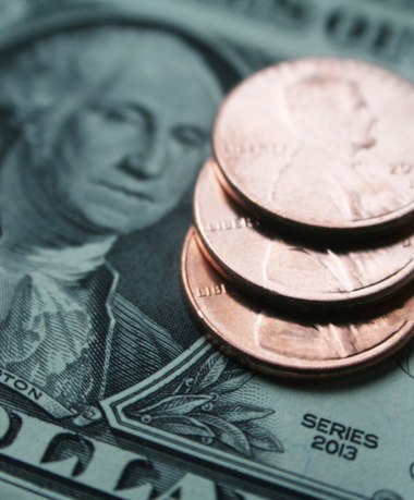 Stack of three pennies on a U.S. dollar bill featuring George Washington. The image accents the economic theme with a close-up perspective.