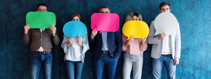 Five people stand against a textured blue wall, each holding colorful speech bubbles in front of their faces, creating a playful and diverse atmosphere.